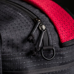 Close-up of black textured GORUCK rucksack zipper pulls and red patterned fabric detail