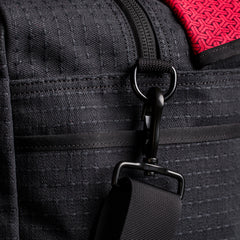 Close-up of durable black GORUCK rucking bag fabric with heavy-duty clip and red patterned strap detail