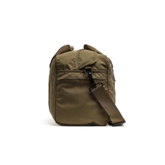 The Kit Bag (Includes Shoulder Strap) in olive green features an adjustable strap and outer pocket, inspired by a classic aviator’s kit bag, shown upright against a white background.