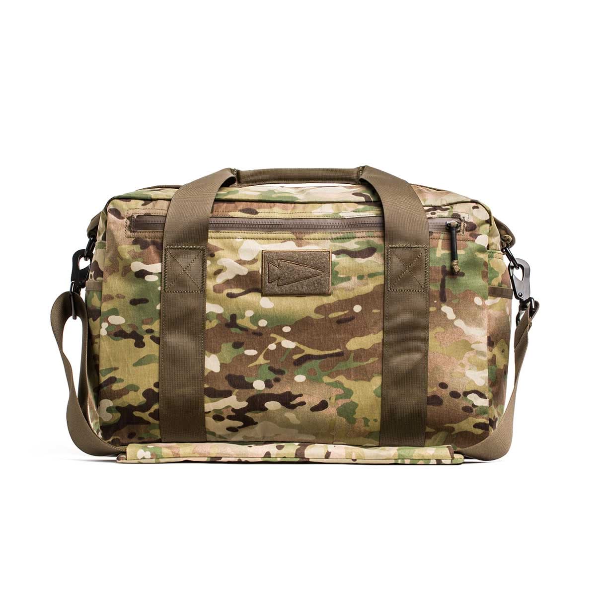 The Kit Bag - X-PAC, inspired by Special Forces gear, features camo print, olive green straps, and a shoulder strap. Shown against a white background.