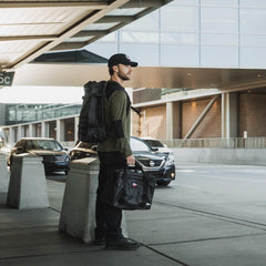 Man at airport curb with black GORUCK Dyneema kitbag and rucksack, ready for travel