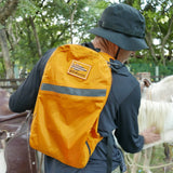 Wearing a black hat and carrying the Packable Bullet Ruck - Ripstop ROBIC® in orange from GORUCK, a person pets a white horse outdoors near trees.