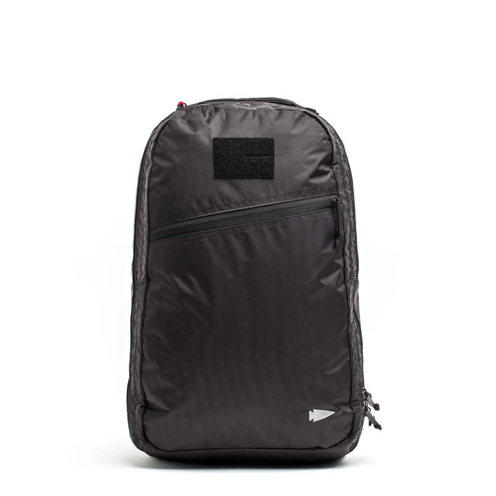The GORUCK Bullet Ruck Double Compartment in black showcases a minimalist design with a front zippered pocket and a small square patch above it. Made from durable Dyneema, it features a subtle arrow emblem near the bottom right and comes with our Lifetime Guarantee for peace of mind.