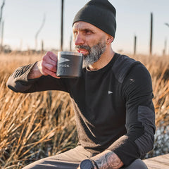 Man wearing black beanie and merino long sleeve shirt drinking from a GORUCK YETI mug in outdoor marsh setting
