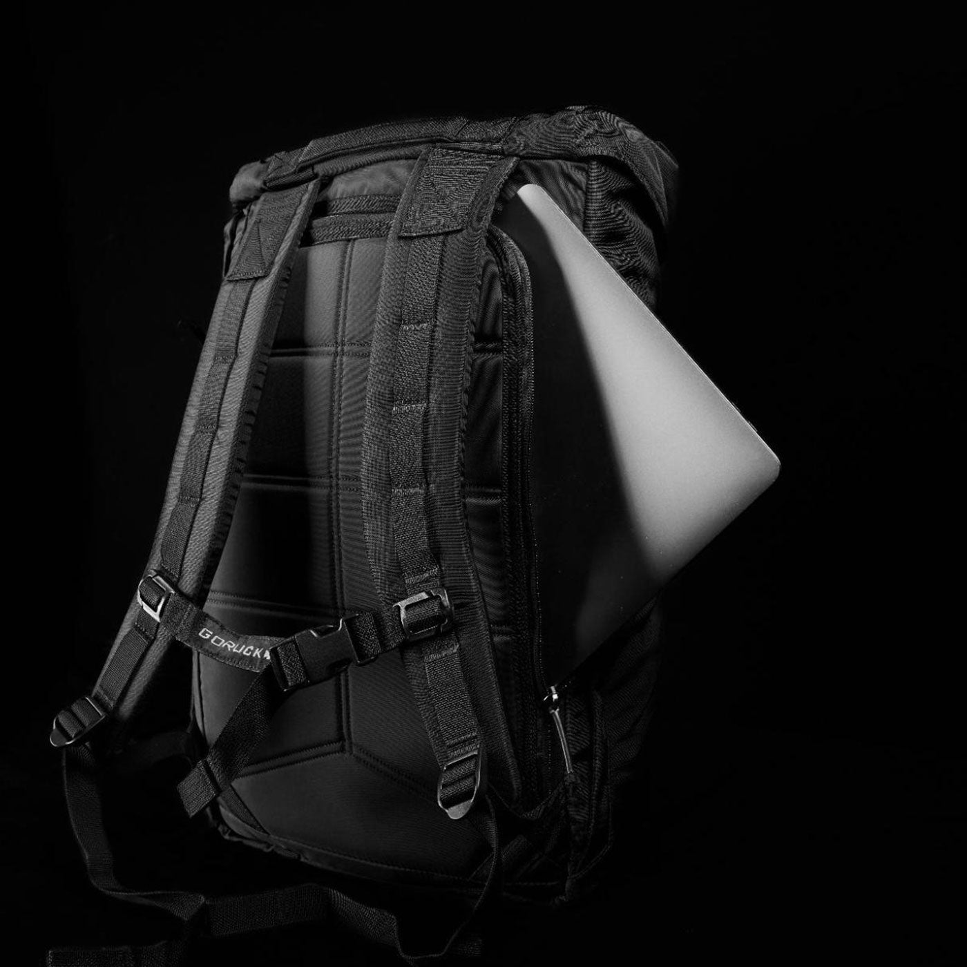 A backpack with a partially visible laptop in the back compartment, set against a black background.