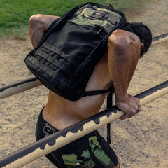 Man performing outdoor dips on metal bars wearing GORUCK camouflage rucking gear backpack and shorts