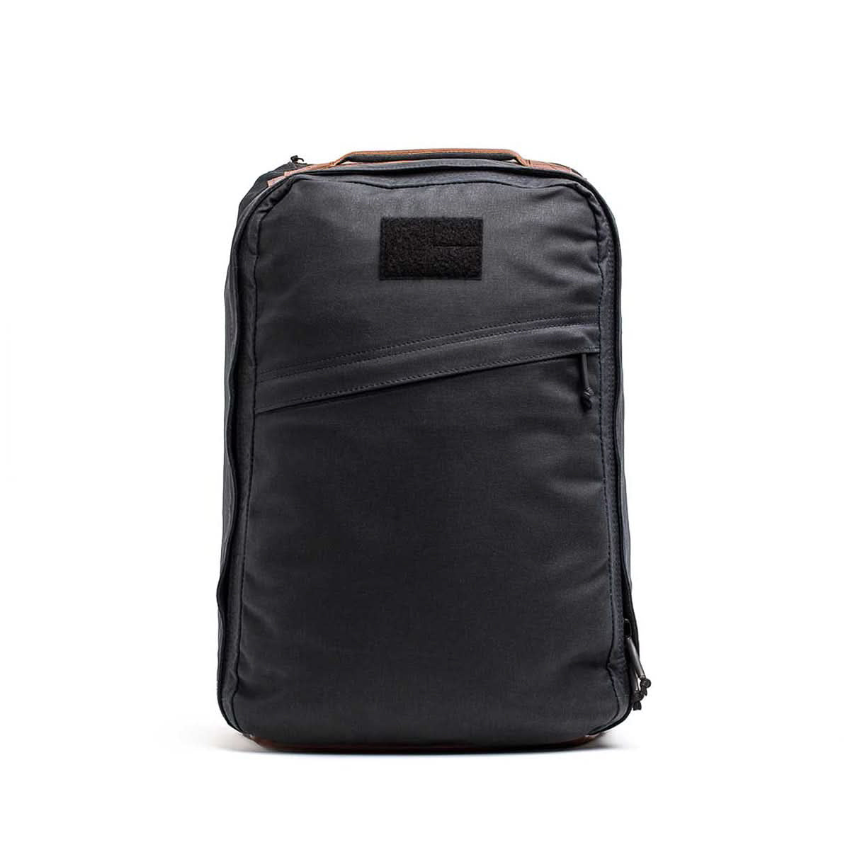 The GR1 USA - Heritage Waxed Canvas is a sleek black canvas backpack featuring a front diagonal zipper pocket and a top handle, displayed against a white background.
