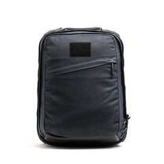 Introducing the GR2 - Waxed Canvas backpack by GORUCK: a sleek, modern black accessory crafted from durable waxed duck canvas. It features a diagonal front zipper pocket and a rectangular patch near the top, enhancing its minimalist design. The smooth fabric and subtle detailing contribute to its refined aesthetic. Photographed against a plain white background, this backpack exudes a touch of heritage retro rucksack style.