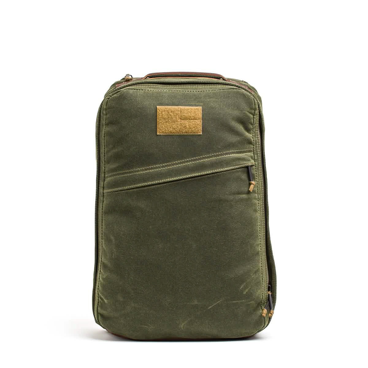 The GR1 USA - Heritage Waxed Canvas rucksack features green waxed canvas, a front zipper pocket, and a brown rectangular patch near the top, drawing inspiration from heritage duck canvas and classic GR1 backpack designs.