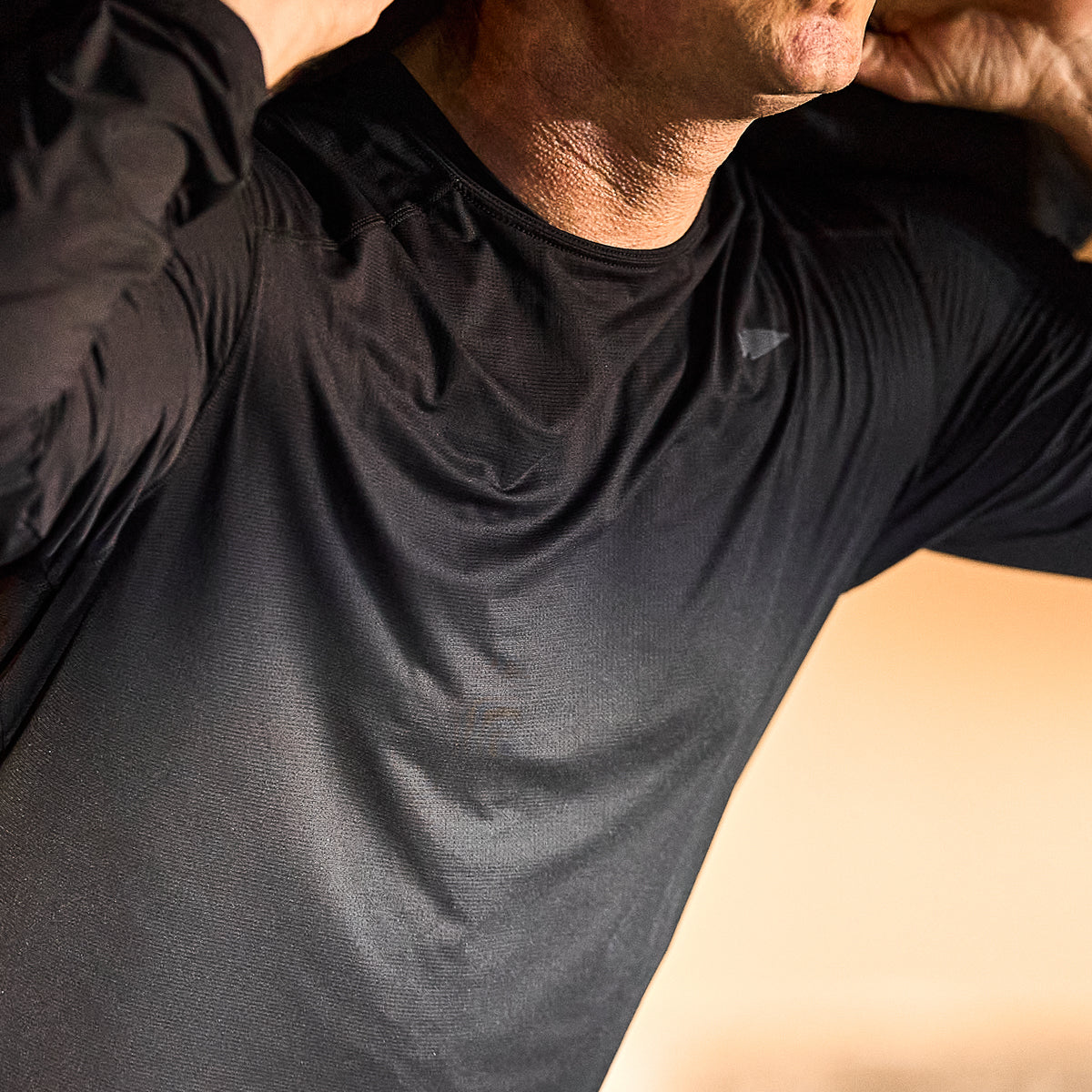 A person in a black Men's USA Long Sleeve Performance Tee - ToughMesh adjusts their collar, highlighting the sleek fit and featherweight feel of this training shirt on the upper torso and neck.