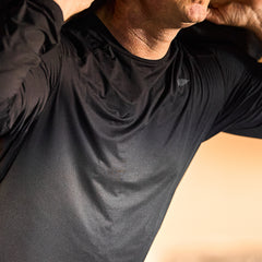 A person in a black Men's USA Long Sleeve Performance Tee - ToughMesh adjusts their collar, highlighting the sleek fit and featherweight feel of this training shirt on the upper torso and neck.