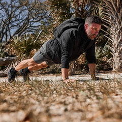 Man doing outdoor push-ups in GORUCK performance full zip longsleeve with rucksack