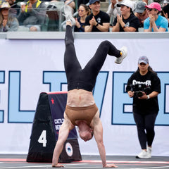 Athlete doing a handstand walk at a CrossFit event, crowd cheering in the background