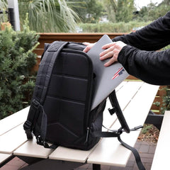 Person placing laptop into black GORUCK Dyneema rucksack on outdoor picnic table