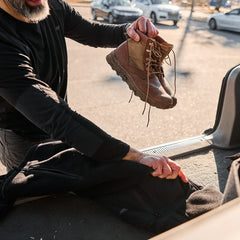 Man holding rugged brown GORUCK boots with coyote mid-top design unloading from car trunk outdoors