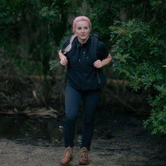 Woman with pink braided hair hiking in forest wearing black vest and rucking boots