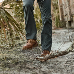 Close-up of rugged brown mid-top boots on a forest trail with green outdoor pants