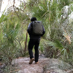 Hiker with GORUCK backpack walking on forest trail surrounded by lush green palm trees