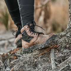 GORUCK Chestnut Black Mid-Top rugged hiking boots with mud on the sole, worn outdoors on uneven terrain