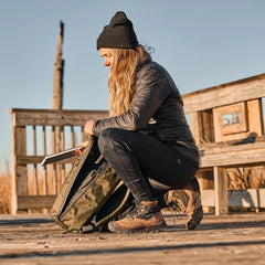 Person wearing black beanie and jacket packing gear into goruck backpack outdoors on wooden platform