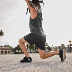 Man wearing black GORUCK ballistic trainers and workout shorts performing a lunge exercise outdoors