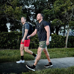 Two men rucking outdoors wearing GORUCK Ballistic Trainers, backpacks, and athletic gear
