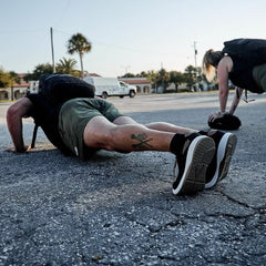 Men wearing GORUCK ballistic trainers and rucksacks doing outdoor push-ups on pavement