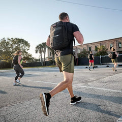 Group rucking outdoors in GORUCK gear and ballistic trainers on pavement under clear sky