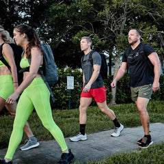 Group of four adults walking outdoors wearing athletic gear and GORUCK backpacks on a sidewalk