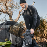 Man wearing black Merino wool base layer by GORUCK at outdoor campsite near tent