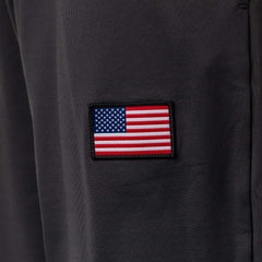 A small American flag patch is sewn onto dark fabric, likely part of the Men’s Training Performance Joggers.