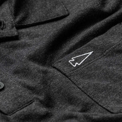 Close-up of a Men's Polo with Pocket - Tri-Blend in black, featuring a white embroidered arrowhead design above the pocket.
