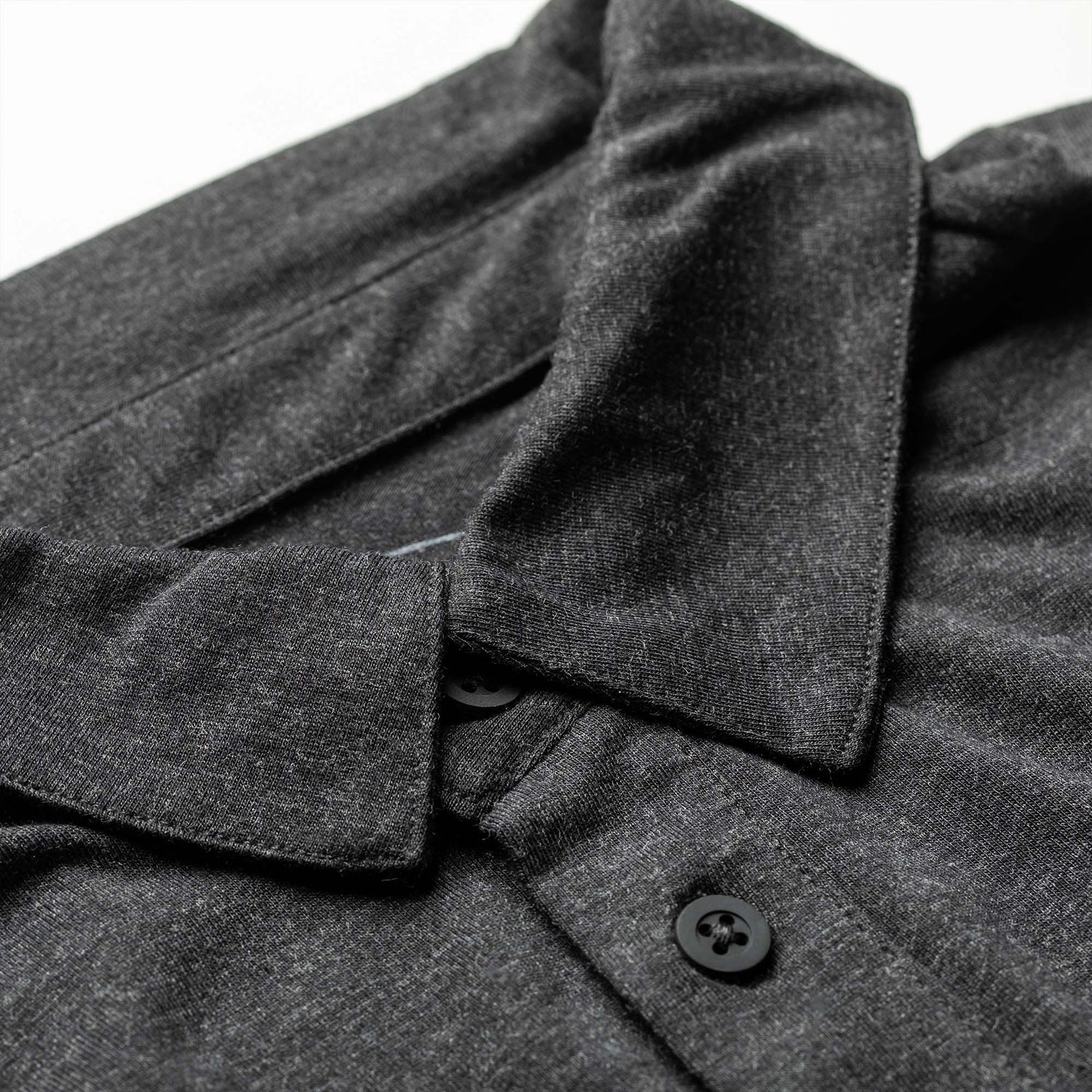 Close-up of the Men's Polo with Pocket - Tri-Blend in dark gray, featuring black buttons, laid flat on a white surface.