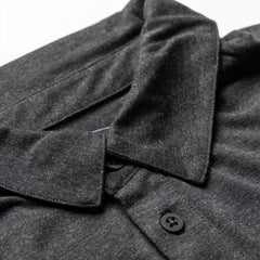 Close-up of the Men's Polo with Pocket - Tri-Blend in dark gray, featuring black buttons, laid flat on a white surface.