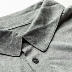 Close-up of a folded Men's Polo with Pocket - Tri-Blend in gray, featuring a collar and black button, displayed on a white background.
