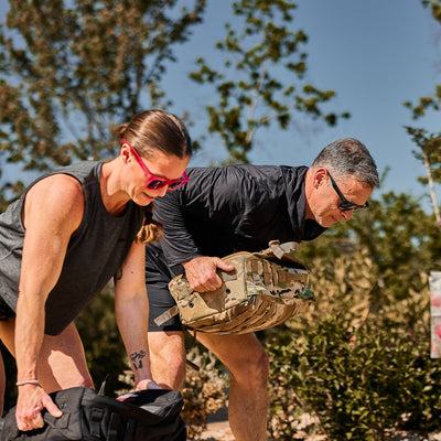 Wearing the Men's USA Sun Hoodie - ToughMesh, two people outdoors lift heavy bags on a sunny day, staying cool and comfortable in breathable performance gear.