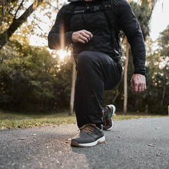 Person wearing black GORUCK joggers and sneakers lunging outdoors on a sunlit forest path