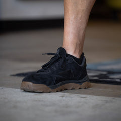 A person stands on a floor with only one black sneaker with brown sole and lower leg visible, wearing Merino Challenge Socks - Ankle (No-Show) made in the USA.