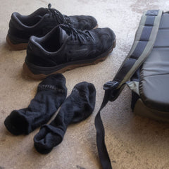 A pair of black sneakers, Merino Challenge Socks - Ankle (No-Show), and a bag on a light, textured floor.