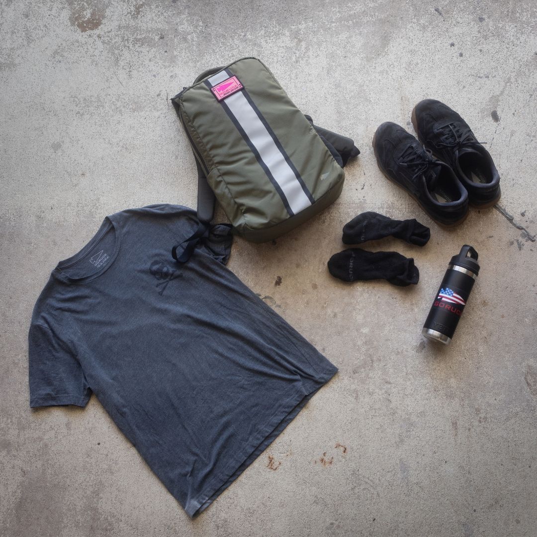 Merino Challenge Socks - Ankle (No-Show), a gray t-shirt, backpack, black shoes, and a water bottle arranged on a concrete floor.