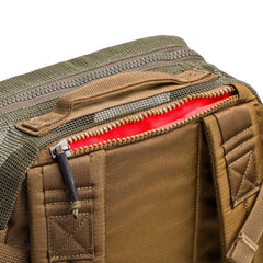 Close-up of the Mesh Ruck, a brown quick-drying backpack, with its zipper partially open to reveal a bright red inner lining.