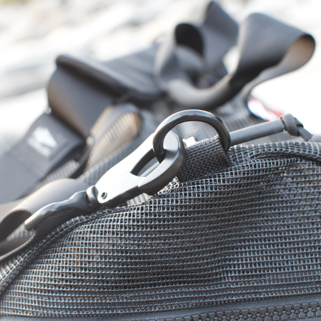 A close-up of a black carabiner clip attached to a mesh pocket on the Mesh Duffel Bag.