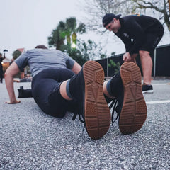 Person doing push-ups on pavement with a coach encouraging during outdoor GORUCK training event