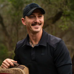 Man outdoors in GORUCK gear, smiling and holding a rucksack with forest background