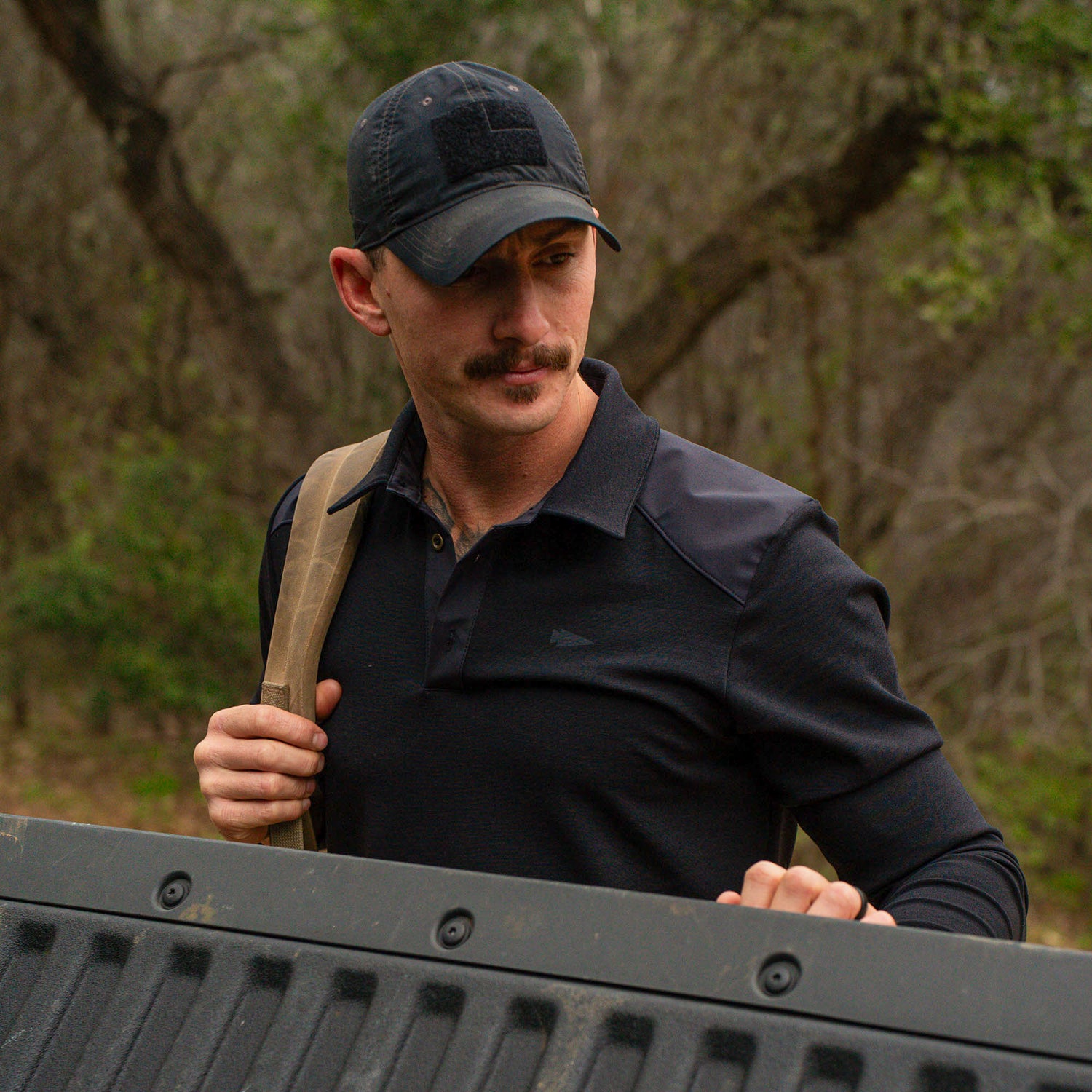 A man with a mustache in a black cap and the Men's Heavy Commando Shirt - Merino Wool stands outdoors by a truck tailgate, holding a strap.