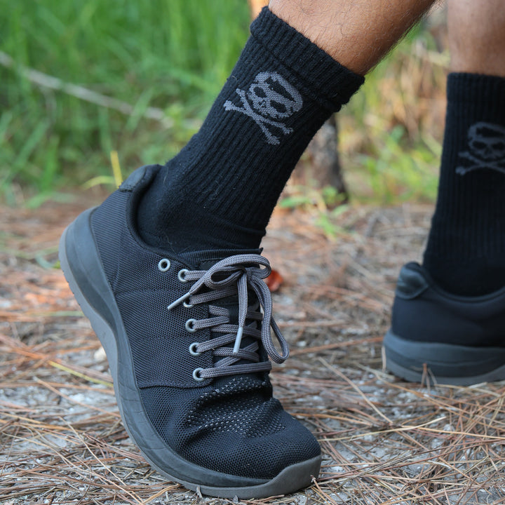 A person's legs wearing Tribe Merino Challenge Socks - Crew in black and black shoes.