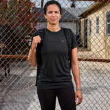 Person wearing GORUCK black rucking shirt and backpack standing by chain link fence outdoors