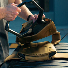 A person fits a hexagonal weight into a tan Rucking Weight Vest on top of a tire—ideal for rucking with curved ruck plates.