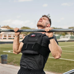 Man doing pull-ups outdoors wearing GORUCK weighted vest, athletic training gear
