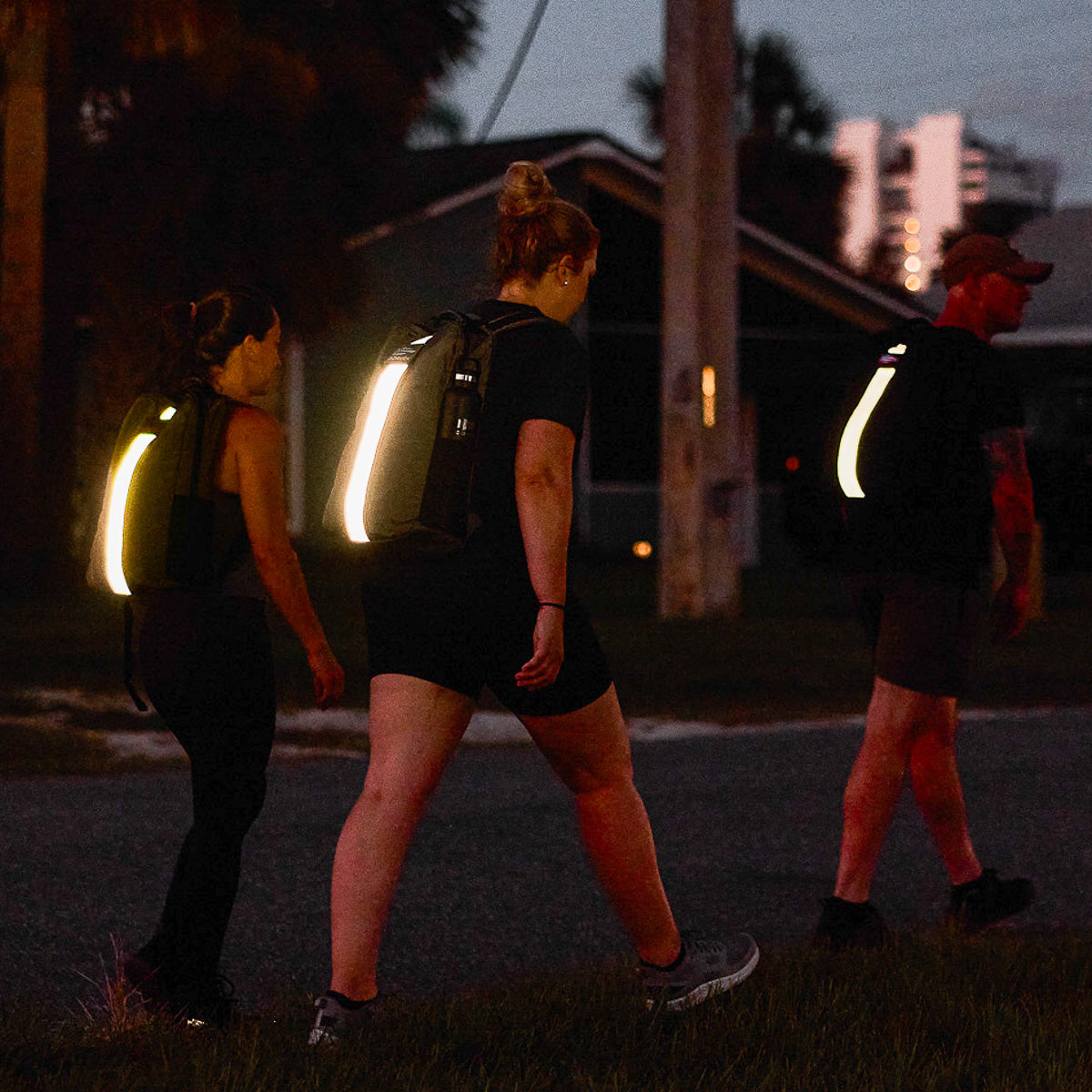Three people walking at dusk with backpacks featuring bright reflective strips for visibility.